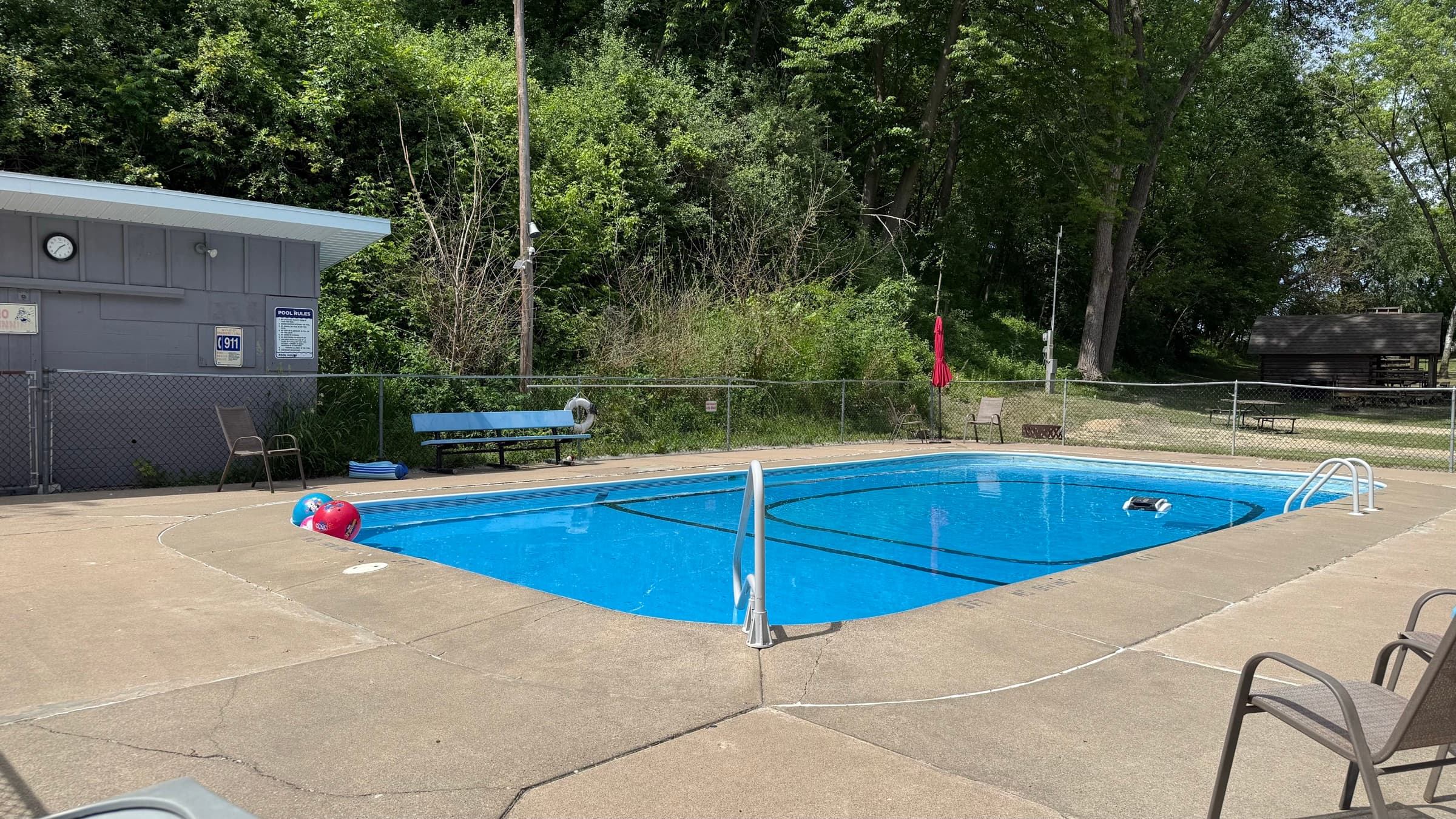 The outdoor swimming pool at Camp Everyday Winona, a fenced in-ground pool with a concrete sun deck and poolside seating set against the wooded hillside